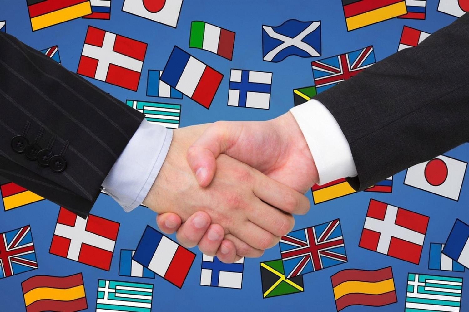 Handshake over a background of world flags representing cross-border business partnership checks